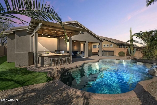 pool at dusk with a hot tub, pool water feature, an outdoor bar, and a patio