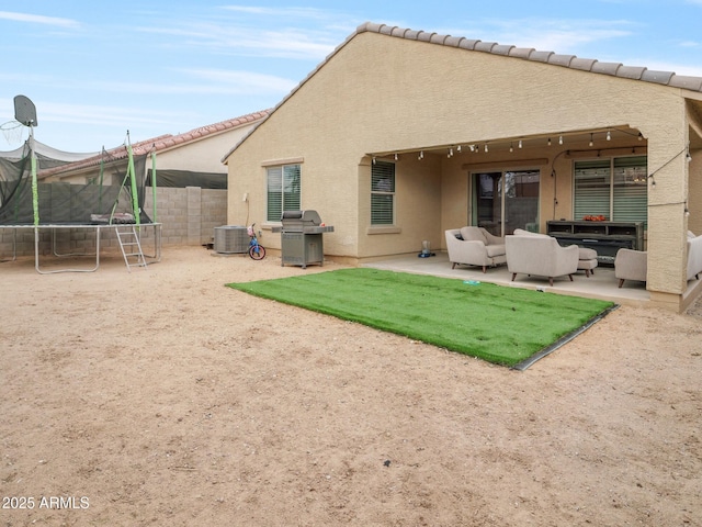 rear view of property with stucco siding, an outdoor living space, a trampoline, fence, and a patio area