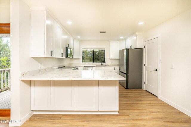 kitchen with stainless steel appliances, kitchen peninsula, sink, light stone countertops, and light hardwood / wood-style floors