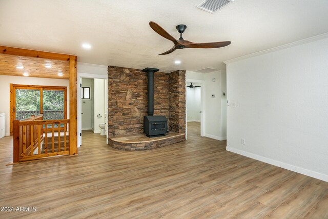 unfurnished living room featuring light wood-type flooring, ceiling fan, a wood stove, and crown molding