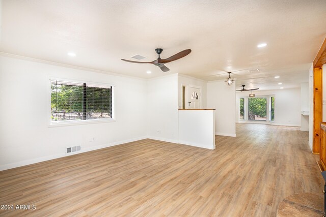 unfurnished living room featuring a wealth of natural light, ceiling fan, ornamental molding, and light wood-type flooring