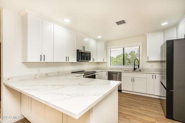 kitchen featuring light stone countertops, stainless steel appliances, sink, kitchen peninsula, and light wood-type flooring