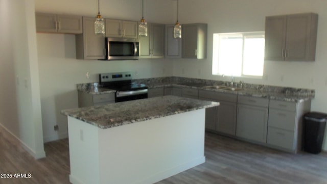 kitchen featuring light stone counters, stainless steel appliances, wood finished floors, a sink, and a center island