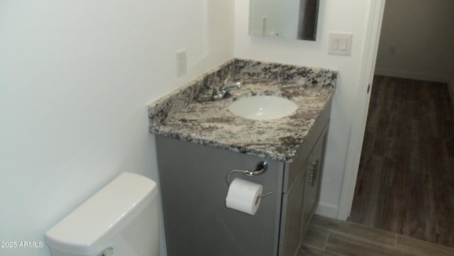 half bathroom featuring toilet, baseboards, wood finished floors, and vanity