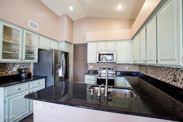 kitchen featuring a textured ceiling, dark stone countertops, stainless steel appliances, and vaulted ceiling