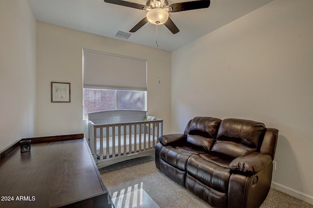 bedroom featuring a nursery area, light colored carpet, and ceiling fan