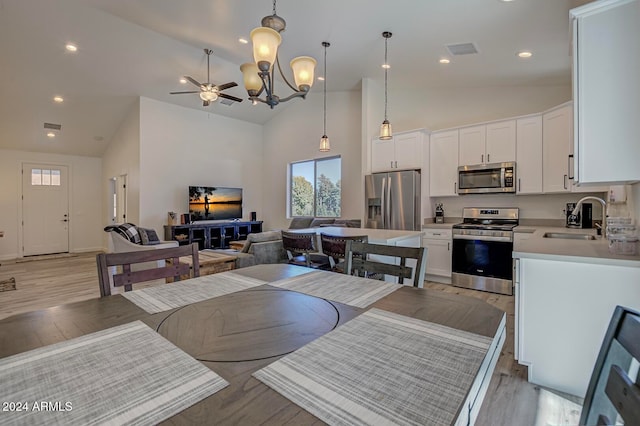 dining area featuring high vaulted ceiling, light wood-type flooring, sink, and ceiling fan with notable chandelier