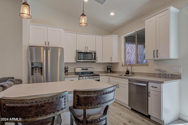 kitchen with stainless steel appliances, vaulted ceiling, sink, pendant lighting, and white cabinetry