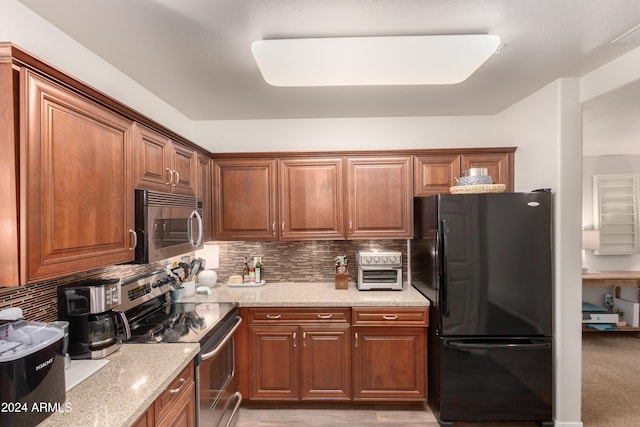 kitchen featuring brown cabinetry, tasteful backsplash, light stone counters, and stainless steel appliances