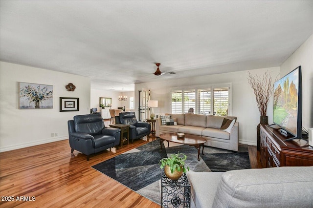 living area with baseboards, wood finished floors, and ceiling fan with notable chandelier
