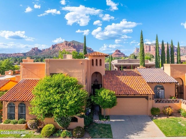 mediterranean / spanish house with concrete driveway, a tiled roof, a mountain view, and stucco siding