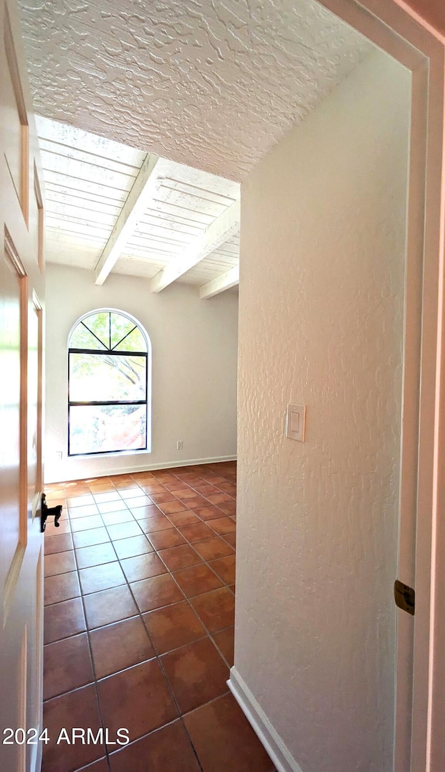 interior space with a textured ceiling, a textured wall, baseboards, tile patterned floors, and beamed ceiling