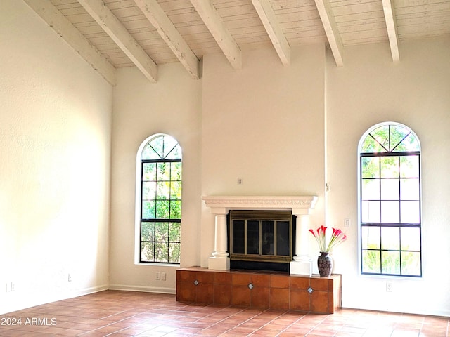 unfurnished living room with beam ceiling, a high ceiling, a glass covered fireplace, light tile patterned flooring, and wooden ceiling