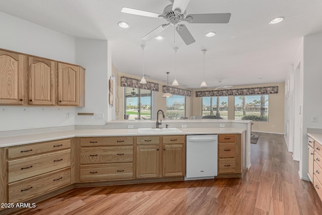 kitchen with light brown cabinets, dishwasher, a peninsula, and a sink