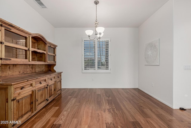 unfurnished dining area with a chandelier, visible vents, baseboards, and wood finished floors