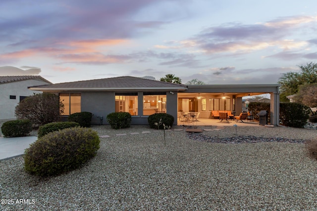 back of house at dusk with a patio area and stucco siding