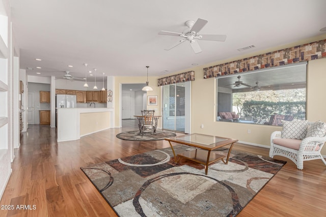 living room with light wood-style flooring, visible vents, ceiling fan, and baseboards