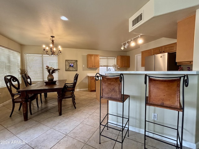 kitchen with an inviting chandelier, light tile patterned flooring, kitchen peninsula, a breakfast bar area, and stainless steel fridge