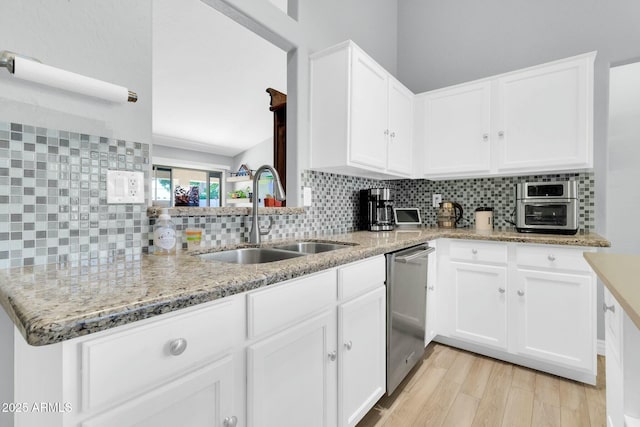 kitchen featuring light wood-style floors, stainless steel dishwasher, light stone counters, a sink, and backsplash