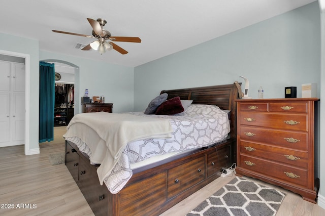 bedroom featuring a closet, light wood-style flooring, a ceiling fan, visible vents, and arched walkways