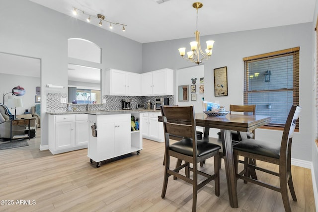 dining room featuring visible vents, baseboards, a high ceiling, a chandelier, and light wood-style floors