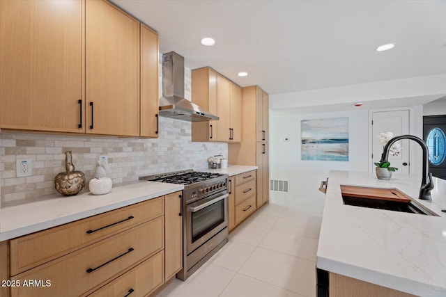 kitchen featuring high end stove, ventilation hood, light brown cabinets, and sink