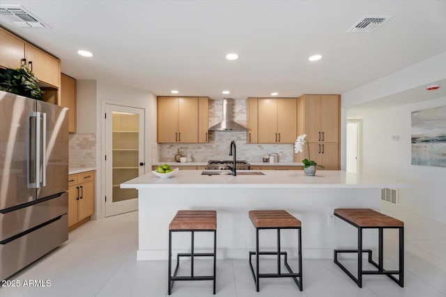 kitchen featuring a breakfast bar, light brown cabinetry, wall chimney exhaust hood, high end refrigerator, and backsplash