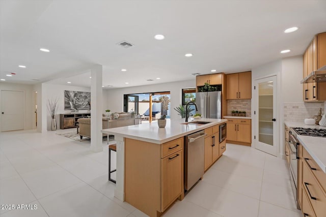 kitchen with tasteful backsplash, light tile patterned floors, a breakfast bar area, a center island with sink, and appliances with stainless steel finishes