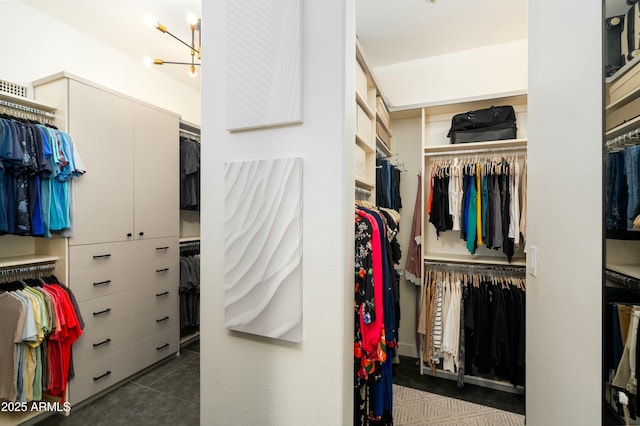 walk in closet with a notable chandelier and dark tile patterned flooring