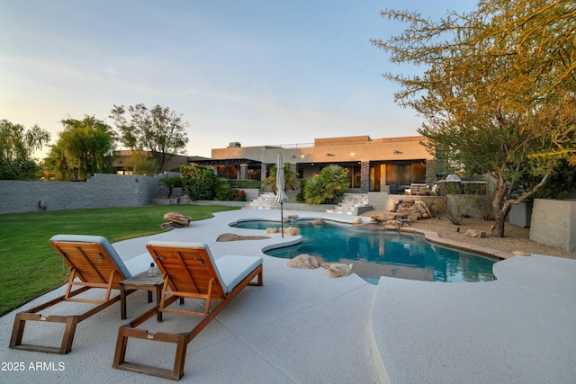 pool at dusk with a patio, exterior kitchen, and a lawn