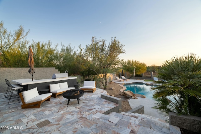 pool at dusk with an outdoor bar, a fire pit, and a patio