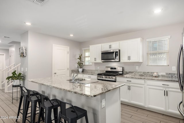 kitchen featuring white cabinets, light wood-style flooring, appliances with stainless steel finishes, light stone counters, and a kitchen island with sink