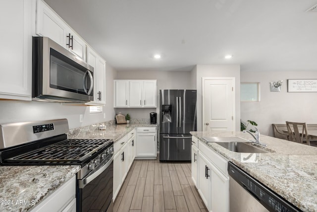 kitchen with appliances with stainless steel finishes, wood tiled floor, white cabinetry, and a sink