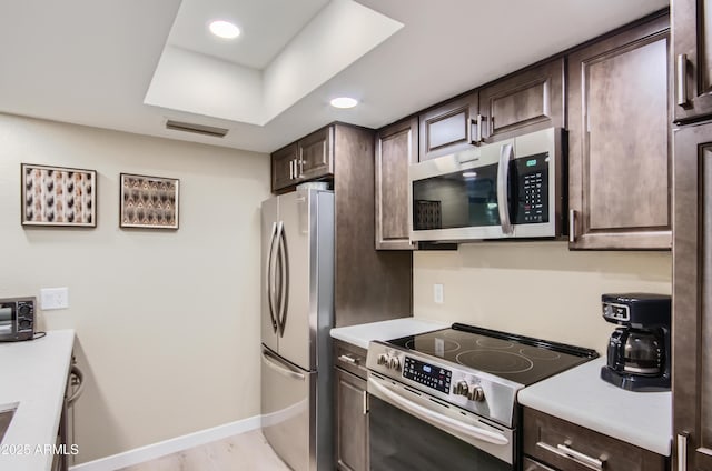 kitchen with dark brown cabinetry, stainless steel appliances, and light wood-type flooring