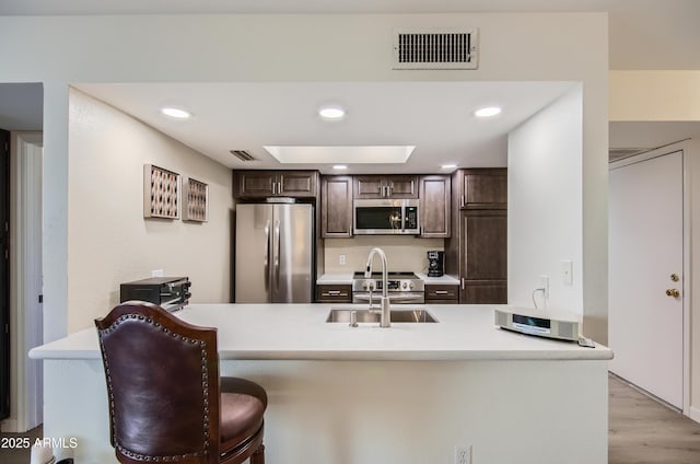 kitchen with dark brown cabinets, stainless steel appliances, kitchen peninsula, and a breakfast bar