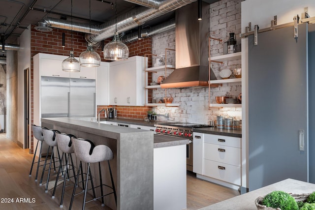 kitchen featuring a barn door, white cabinetry, premium range, and wall chimney range hood