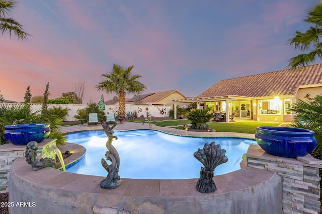 pool at dusk with an outdoor hot tub, a patio, and a lawn