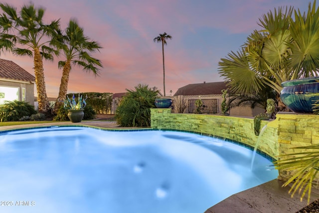 pool at dusk featuring pool water feature