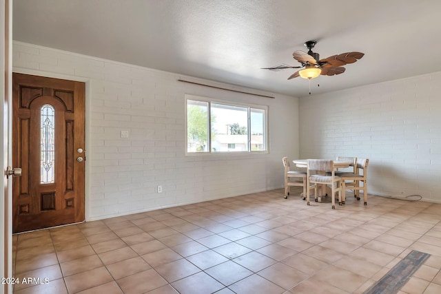 unfurnished dining area featuring ceiling fan, light tile patterned floors, brick wall, and a textured ceiling