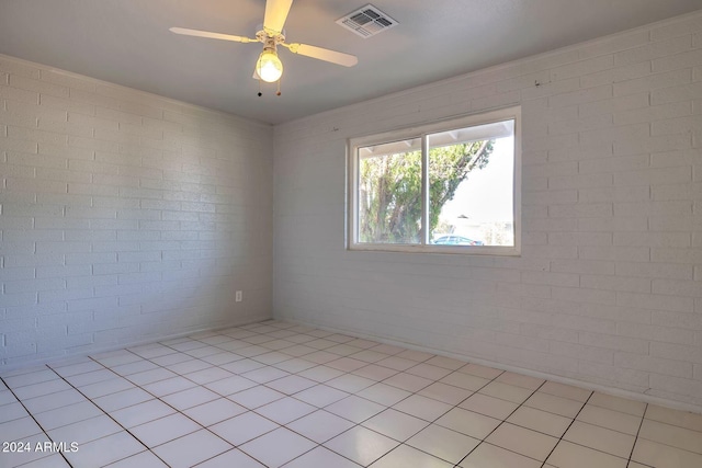 empty room featuring ceiling fan, light tile patterned flooring, and brick wall