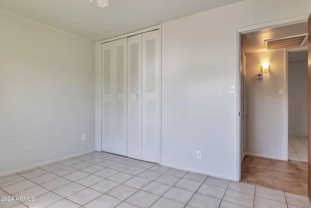 unfurnished bedroom with light tile patterned floors, a closet, and brick wall