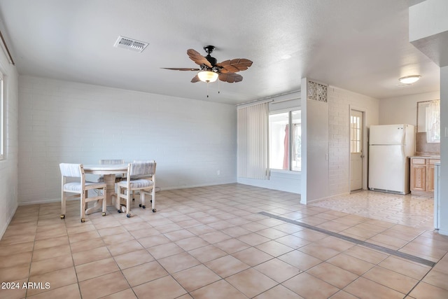 unfurnished dining area with light tile patterned floors, a textured ceiling, ceiling fan, and brick wall