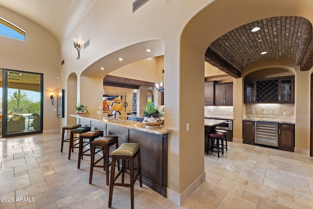 bar featuring beverage cooler, stone tile floors, backsplash, and visible vents