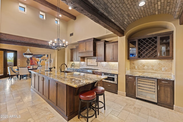 kitchen with beverage cooler, high vaulted ceiling, stone tile flooring, and stainless steel gas stovetop