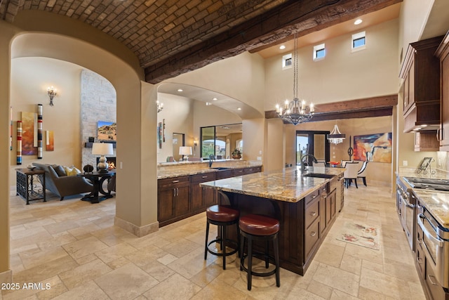 kitchen featuring a breakfast bar area, double oven range, a towering ceiling, a sink, and stone tile floors