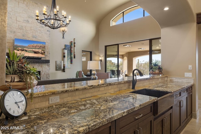 kitchen featuring arched walkways, dark brown cabinets, a sink, dark stone countertops, and a notable chandelier
