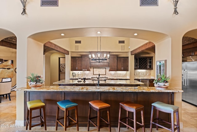 kitchen with a spacious island, dark brown cabinetry, stainless steel built in refrigerator, and visible vents