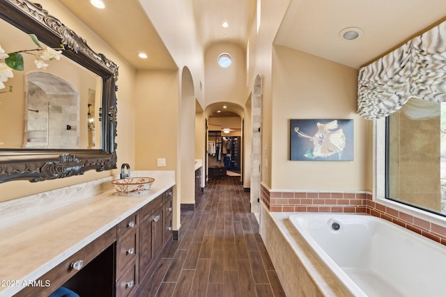 full bathroom featuring vanity, a walk in closet, recessed lighting, a bath, and vaulted ceiling
