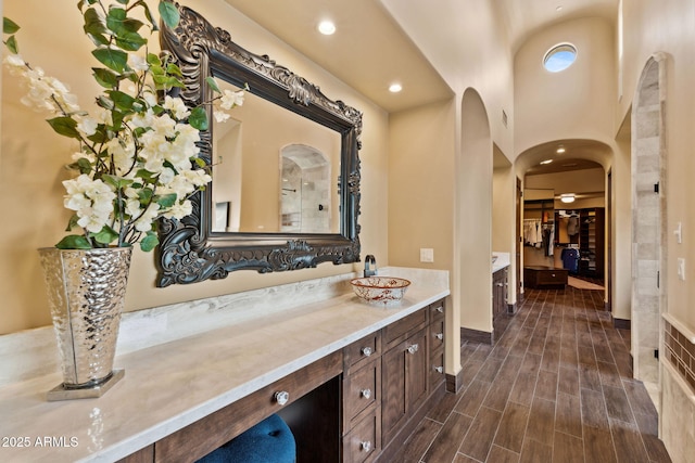 bathroom with a walk in closet, vanity, recessed lighting, baseboards, and wood finished floors