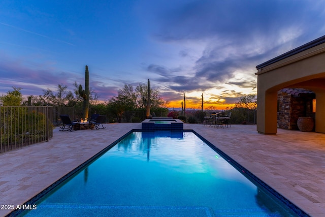 pool at dusk featuring a pool with connected hot tub, fence, a fire pit, and a patio area